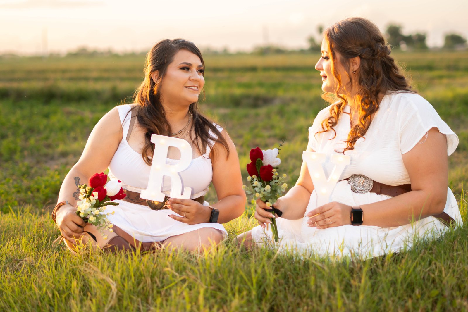 Karina y Yazmín en un campo al atardecer, sosteniendo las letras R y Y